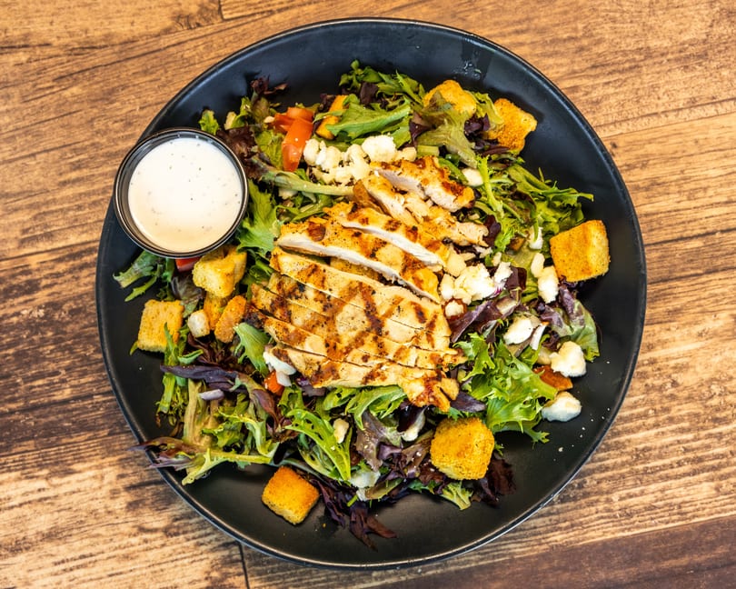 Grilled chicken salad with mixed greens, croutons, feta cheese, tomatoes, and a side of ranch dressing.