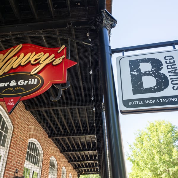 Two hanging signs, one for "Harvey's Bar & Grill" and another for "B Squared Bottle Shop & Tasting Room".