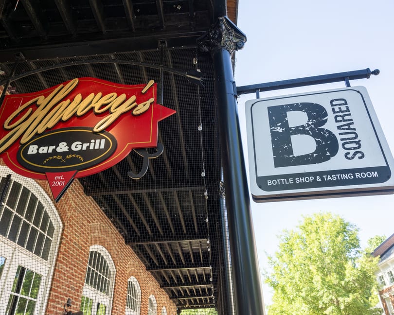 Two hanging signs, one for "Harvey's Bar & Grill" and another for "B Squared Bottle Shop & Tasting Room".