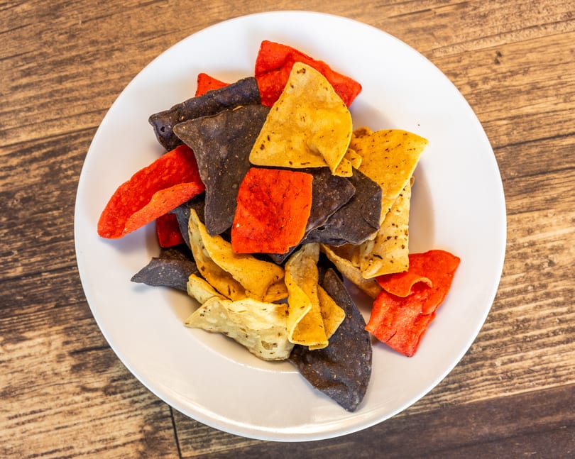 A white plate filled with red, blue, and yellow tortilla chips on a wooden table.