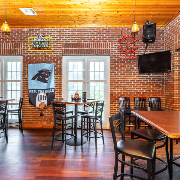 Interior of a casual bar with brick walls, wooden floors, high-top tables, and Carolina Panthers decor.