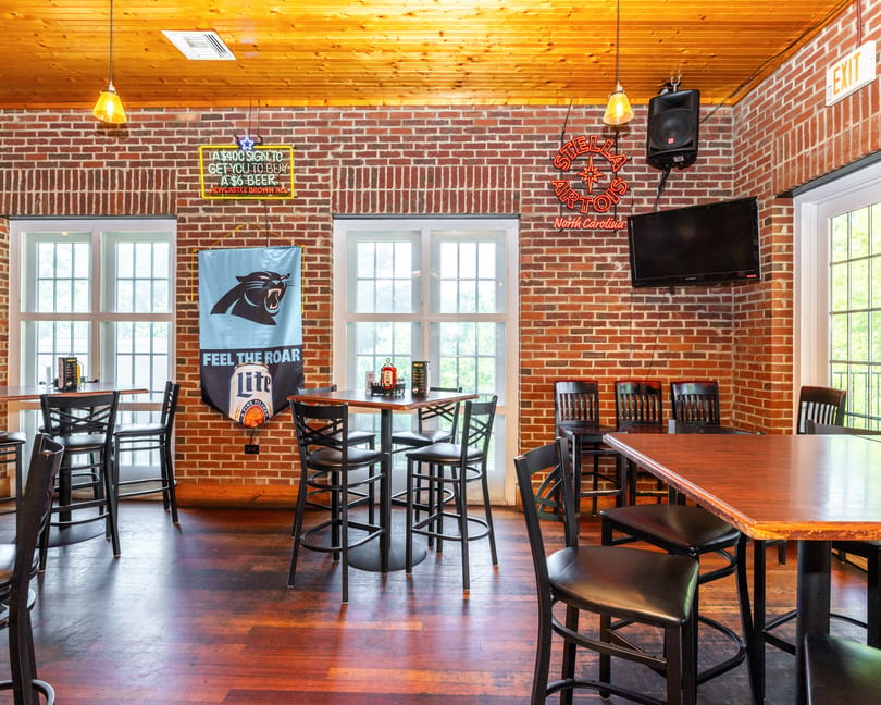 Interior of a casual bar with brick walls, wooden floors, high-top tables, and Carolina Panthers decor.