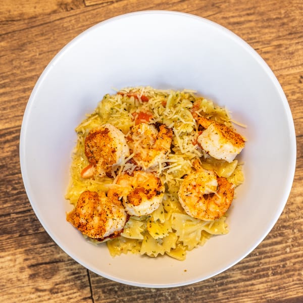 Shrimp scampi with bow-tie pasta, diced tomatoes, and shredded cheese in a white bowl.