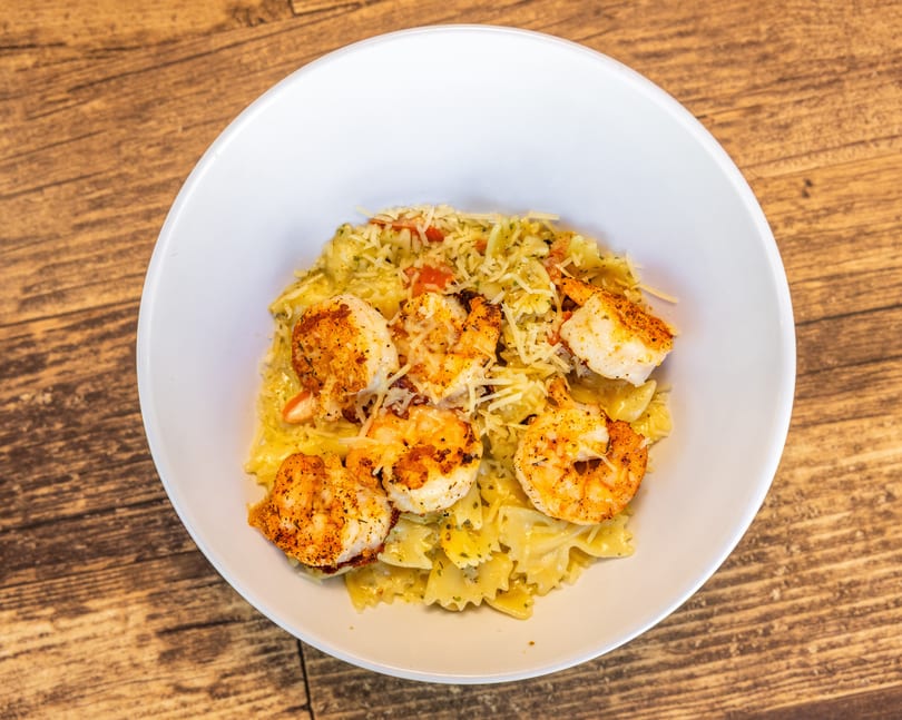 Shrimp scampi with bow-tie pasta, diced tomatoes, and shredded cheese in a white bowl.