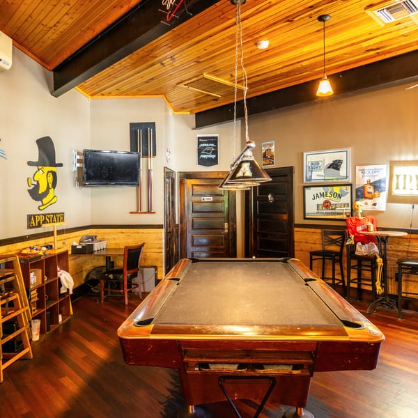 A rustic game room with a pool table, wooden ceiling, and sports-themed decor.