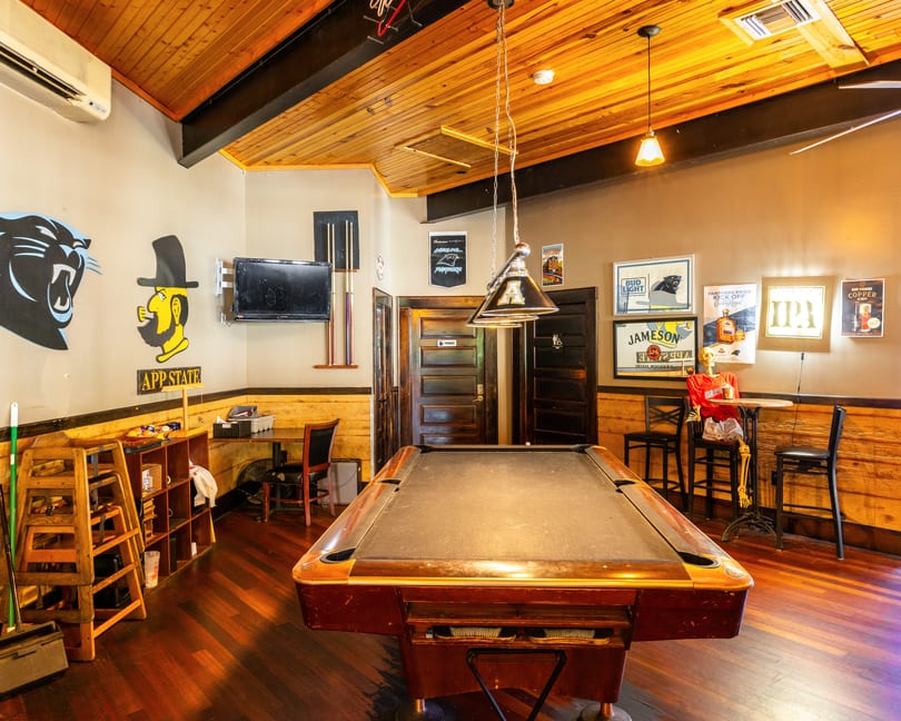 A rustic game room with a pool table, wooden ceiling, and sports-themed decor.