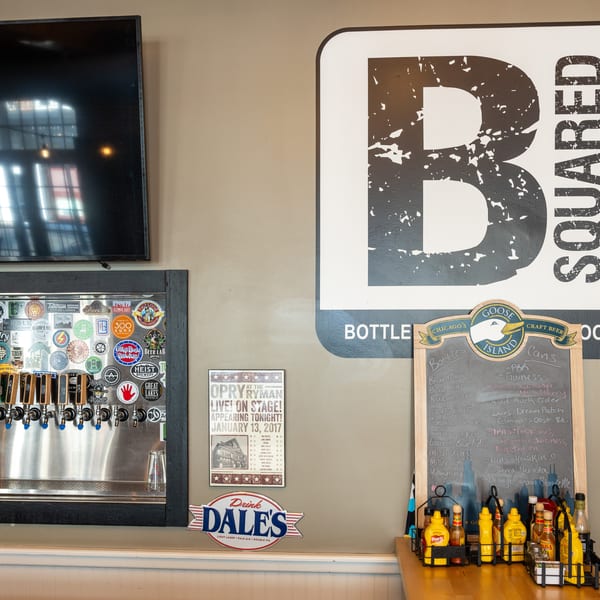 A wall with a large B Squared logo, beer taps, and a chalkboard menu.