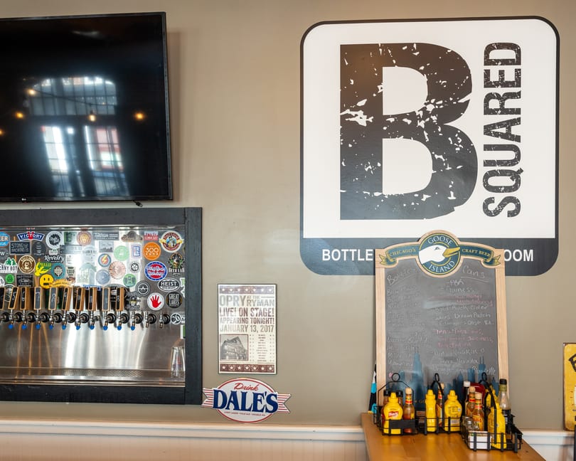 A wall with a large B Squared logo, beer taps, and a chalkboard menu.