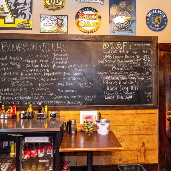 A chalkboard menu displays bourbon, scotch, and draft beer selections above a counter with condiments.
