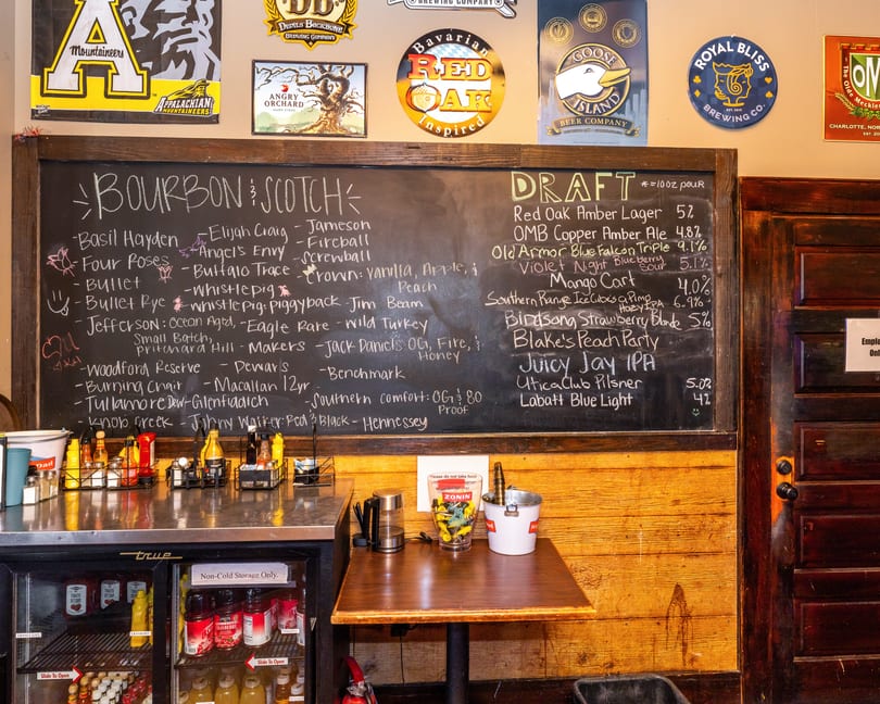 A chalkboard menu displays bourbon, scotch, and draft beer selections above a counter with condiments.