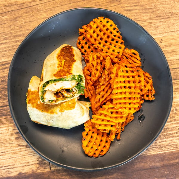 A chicken wrap with green filling and a side of waffle fries on a black plate.