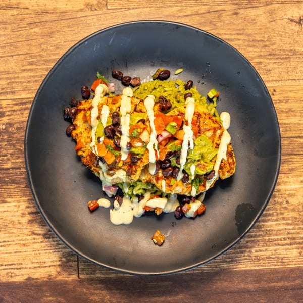 Grilled chicken topped with pico de gallo, black beans, guacamole, and a creamy sauce on green rice.