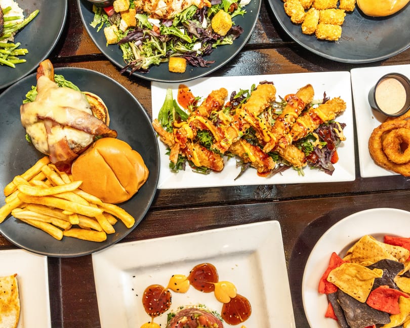 An overhead view of a table laden with various dishes, including a burger, fries, salads, and fried shrimp.
