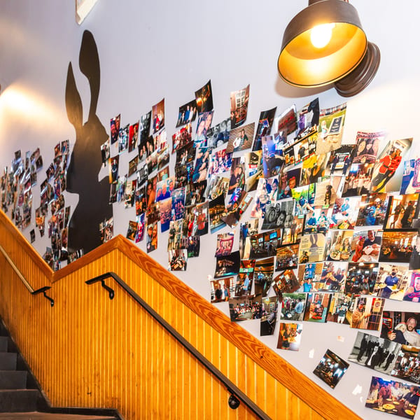 A staircase with wooden railings leads up to a wall covered in numerous framed photos and a large rabbit silhouette.